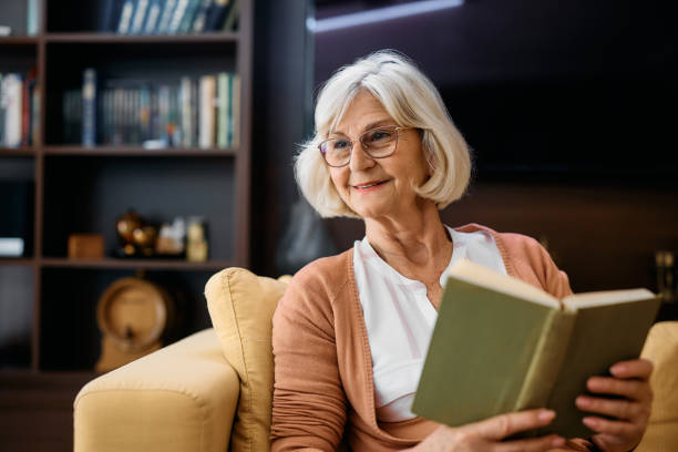 Happy senior woman enjoying while reading book in living room of residential care home.